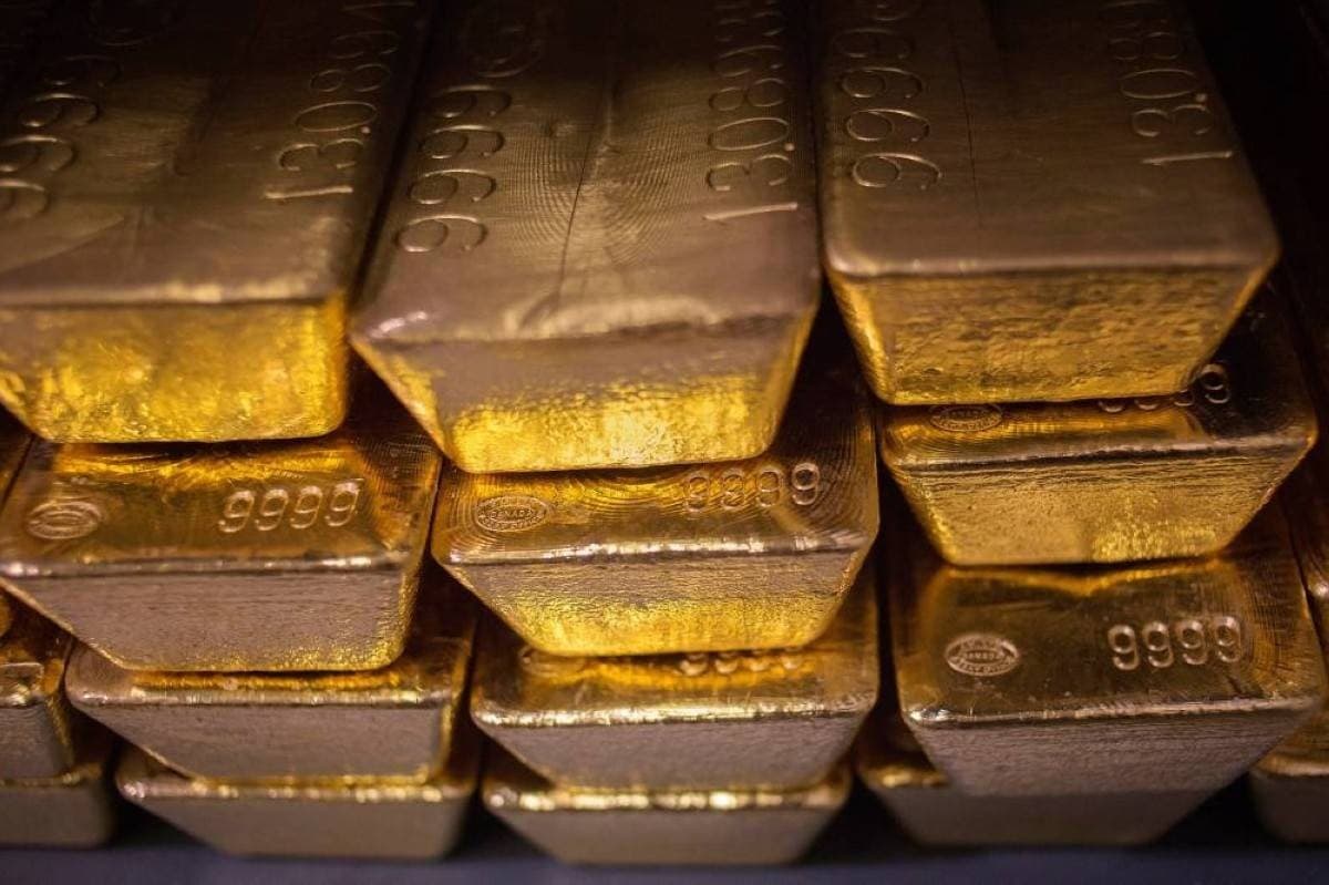 Gold bars and coins displayed against a financial market backdrop, reflecting declining prices amid interest rate hike expectations.