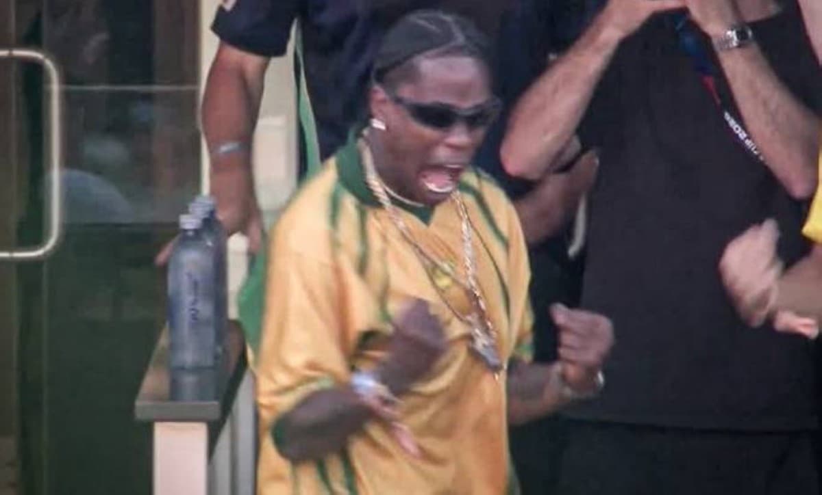 Travis Scott wearing a yellow and green Brazil shirt celebrates in the stands of MetLife Stadium during the 2026 World Cup match between Morocco and Brazil.