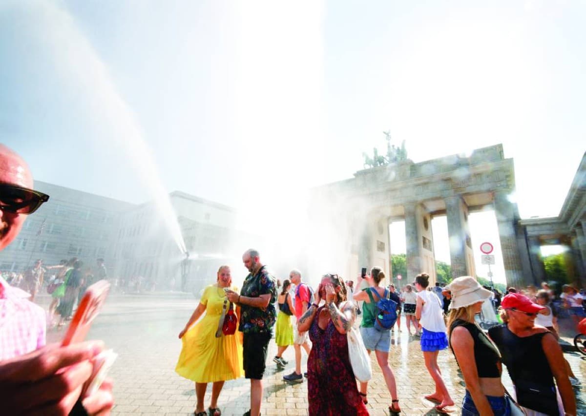 Crowds of people seeking shade and relief during an intense heatwave in a European city, with shimmering heat visible in the background.