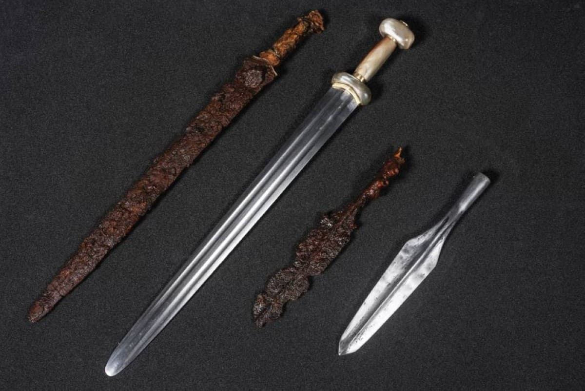 A collection of rare Iron Age artefacts, including an iron sword, bronze cloak pin, glass bead necklace, and bronze rings, discovered in a warrior's grave in Alloa, Scotland.