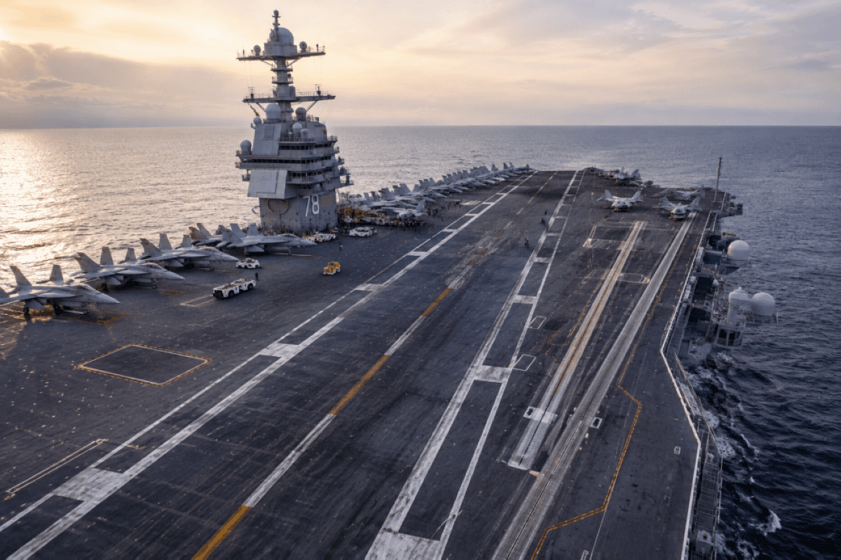 The flight deck of an aircraft carrier at sea, showing its steel non-slip surface with fighter jets positioned for operations.