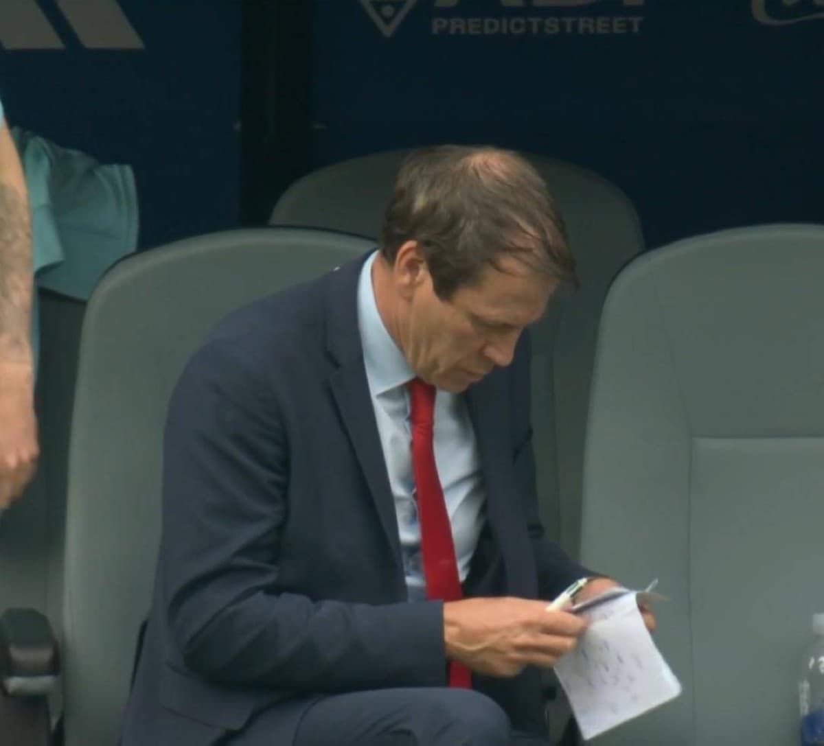 Belgium coach Rudi García sits on the substitutes' bench, pen in hand, writing tactical notes on paper during Belgium's World Cup round-of-32 match against Senegal.