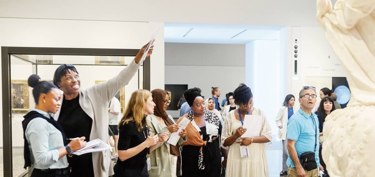 A guided tour group exploring galleries inside Louvre Abu Dhabi during the summer season.