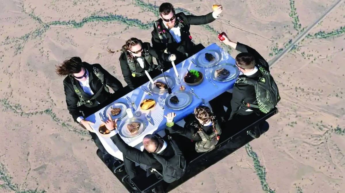Members of the Nitro Circus troupe seated around a dining table during a freefall parachute jump over Utah, with food and tableware assembled mid-air.