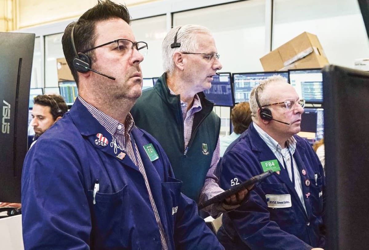 A trader monitors stock market data on screens displaying global equity indices and technology sector movements.