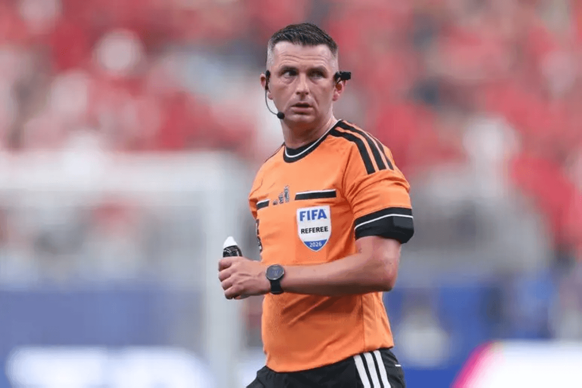 English referee Michael Oliver gestures during a World Cup match, with players from two teams visible on the pitch behind him.