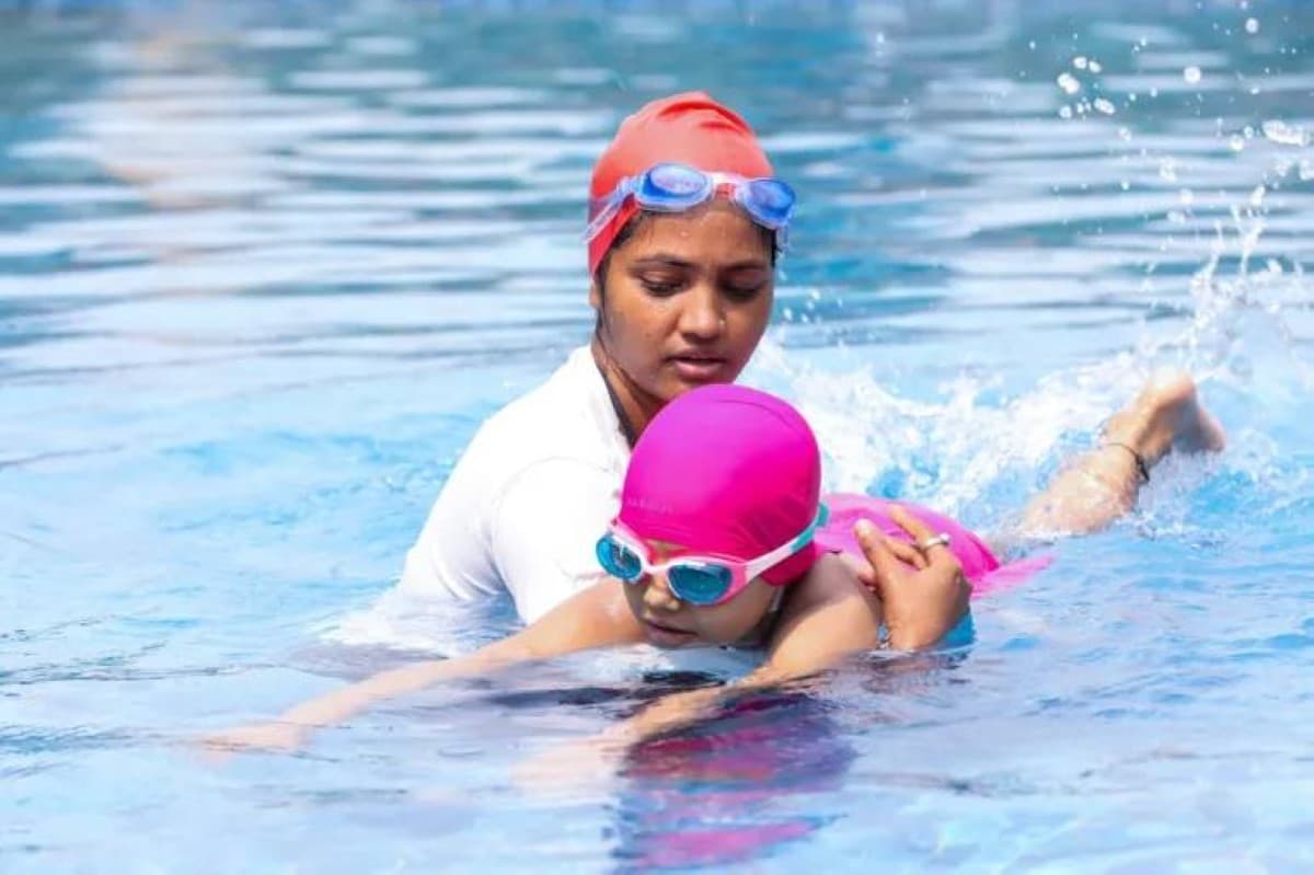 A child near a swimming pool with an adult supervisor watching closely, illustrating water safety during the summer season.