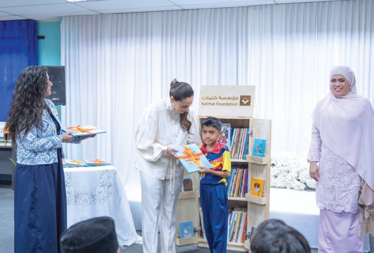 Sheikha Badour bint Sultan Al Qasimi visits a school in Malaysia as part of Kalimat Foundation's mobile library initiative, surrounded by students and officials.