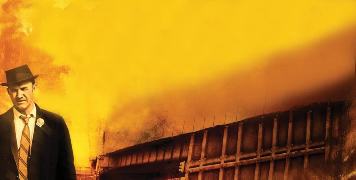 A still from the 1971 film The French Connection showing a car speeding beneath elevated railway tracks in Brooklyn during the film's iconic chase sequence.