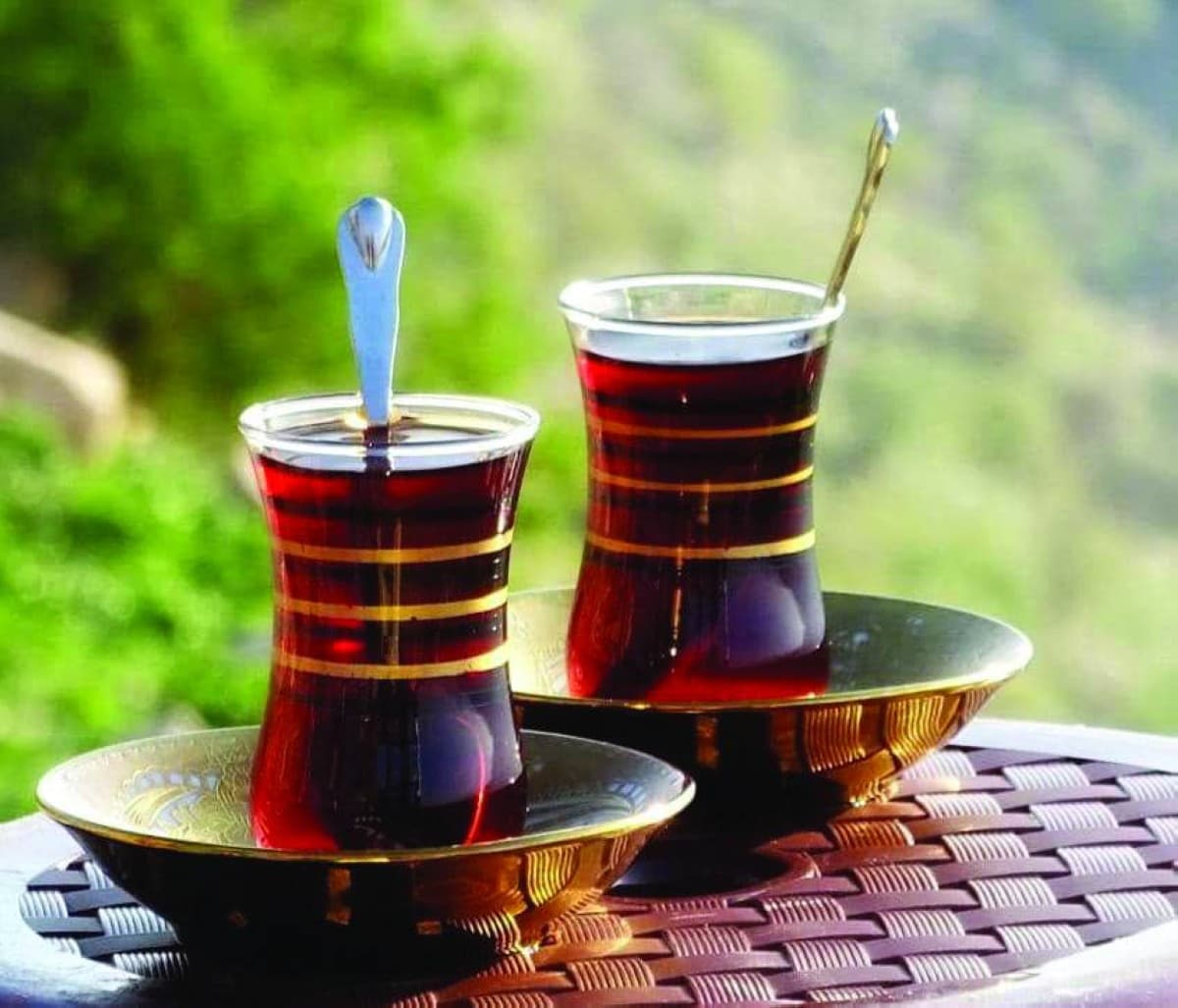 A traditional Iraqi tea setting featuring crystal istakana glasses of dark-brewed chai on small ceramic saucers with gilded teaspoons, evoking Baghdad's rich tea culture.