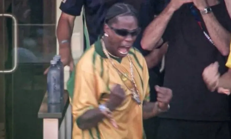 Travis Scott wearing a yellow and green Brazil shirt celebrates in the stands of MetLife Stadium during the 2026 World Cup match between Morocco and Brazil.