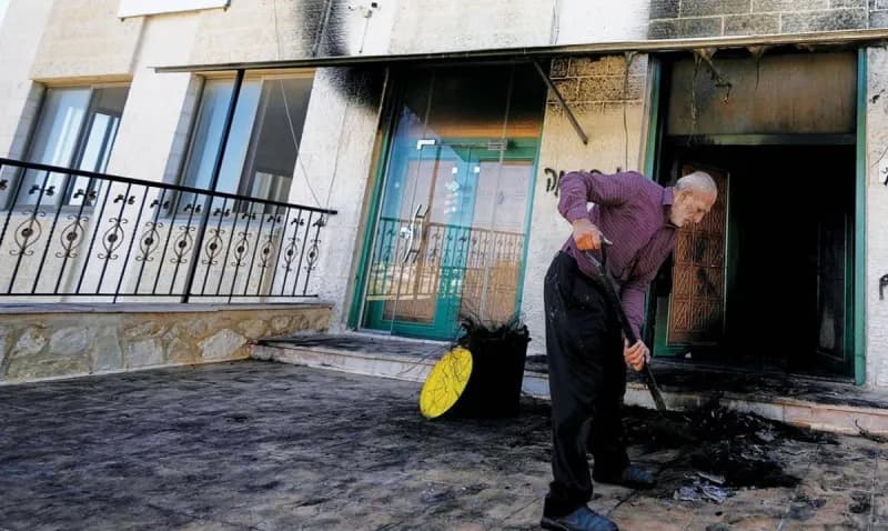 Damage visible on the outer walls of a mosque in the West Bank following an arson attack by Israeli settlers, with burn marks and Hebrew slogans inscribed on the facade.