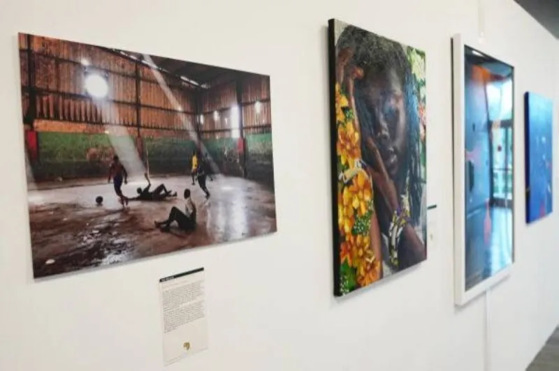 A replica of the FIFA World Cup trophy displayed inside a glass case at the 'Art and the Beautiful Game' exhibition in Miami, surrounded by African football artwork and flags.