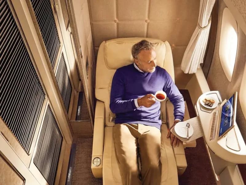 An Emirates airline first-class suite cabin on board an A380 aircraft, featuring a private enclosed suite with luxury seating and mood lighting.