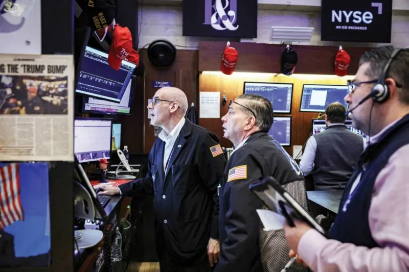 A trader monitors stock market data on multiple screens in a busy financial trading environment.