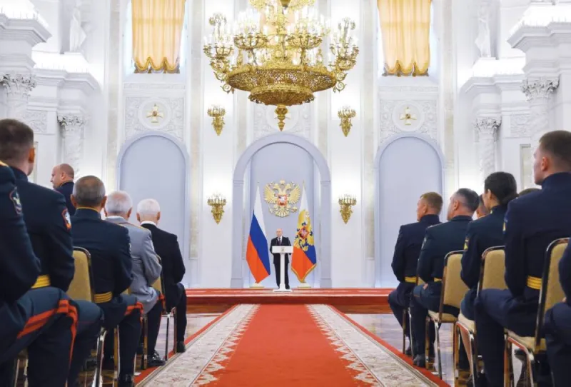 Russian President Vladimir Putin addresses military academy graduates at a ceremony in Moscow, with a Russian flag visible in the background.