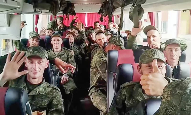 Ukrainian prisoners of war wrapped in blue and yellow Ukrainian flags, smiling and embracing after being freed in a prisoner exchange brokered by the United Arab Emirates.