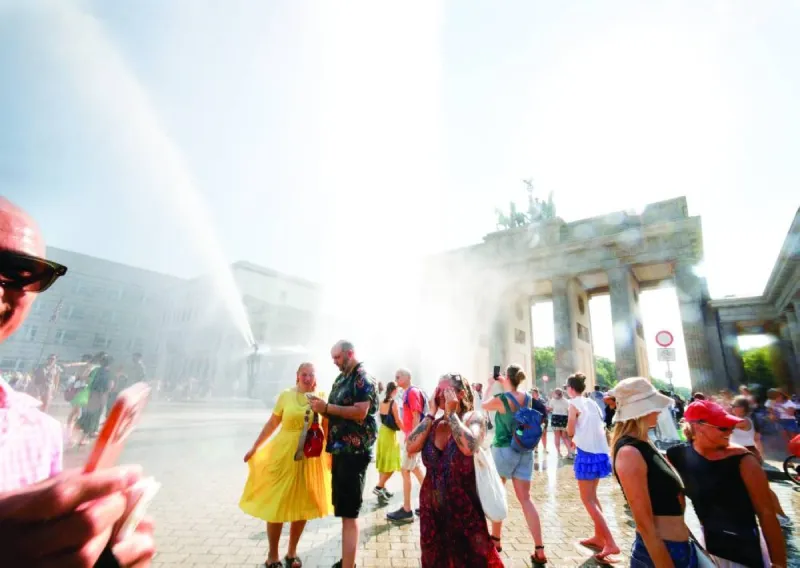Crowds of people seeking shade and relief during an intense heatwave in a European city, with shimmering heat visible in the background.