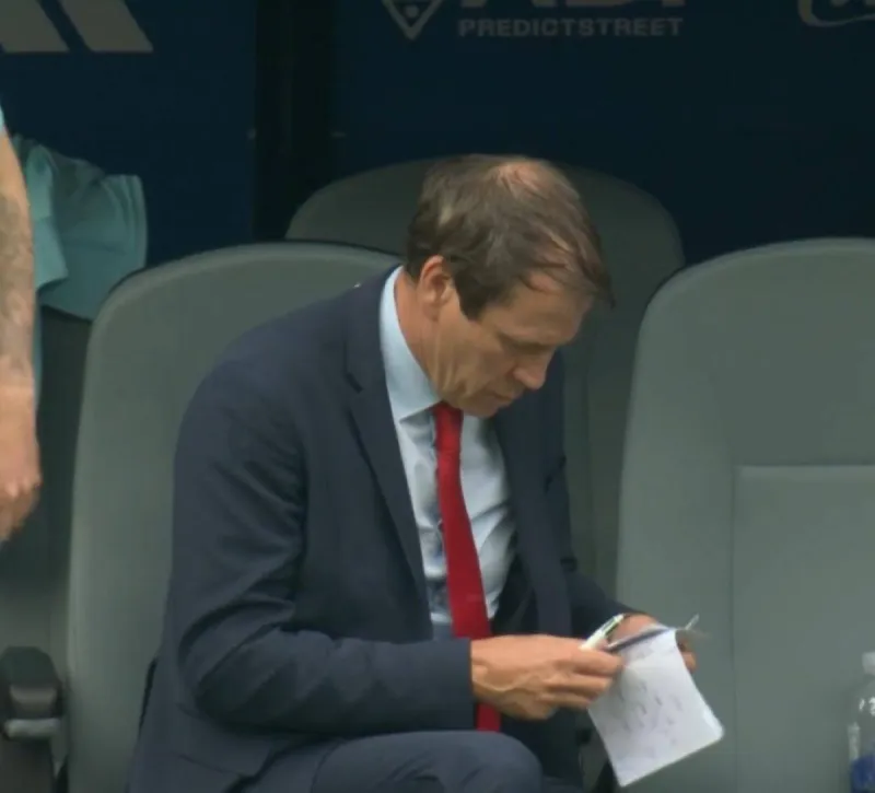 Belgium coach Rudi García sits on the substitutes' bench, pen in hand, writing tactical notes on paper during Belgium's World Cup round-of-32 match against Senegal.