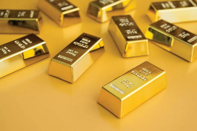 Gold bars and coins displayed alongside a rising US dollar currency symbol, reflecting a decline in gold prices amid a stronger dollar.