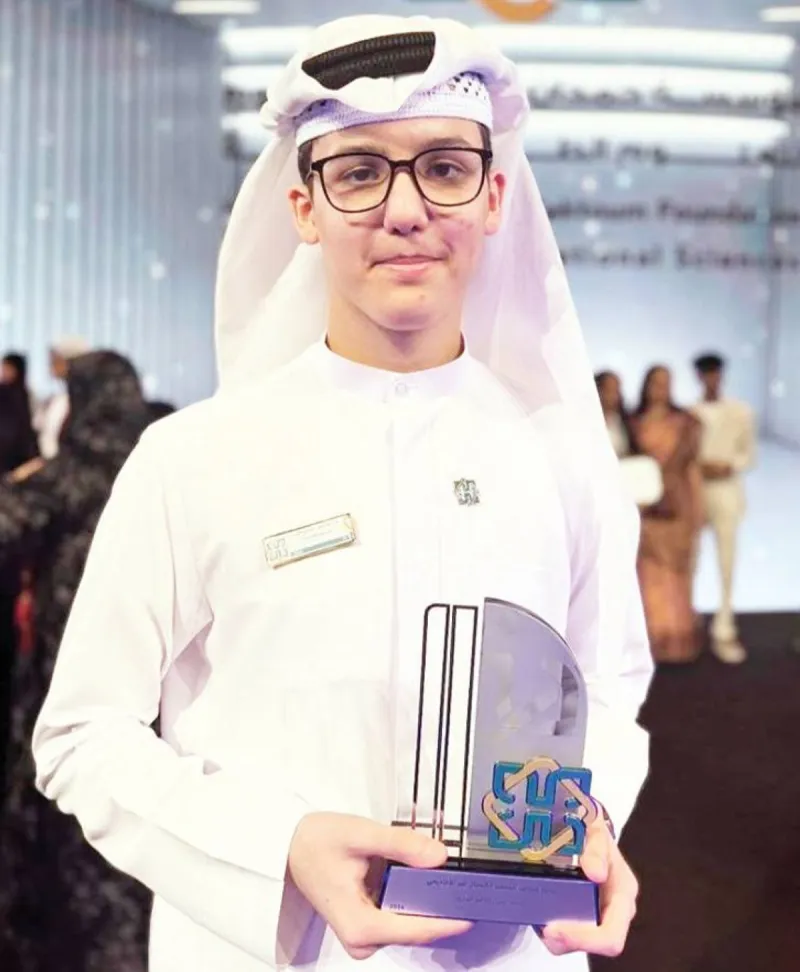 Student Mohamed Yahya stands beside his green energy innovation projects displayed at a school exhibition.