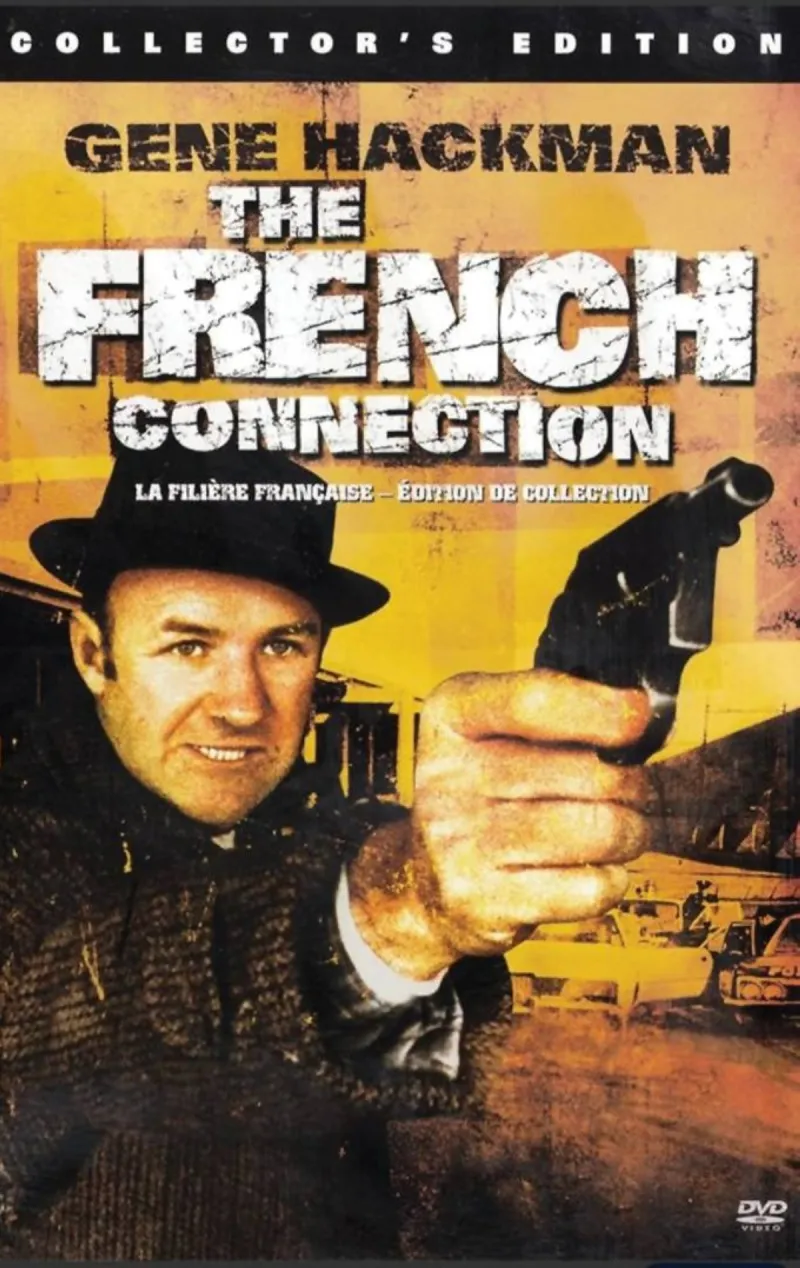 A still from the 1971 film The French Connection showing a car speeding beneath elevated railway tracks in Brooklyn during the film's iconic chase sequence.